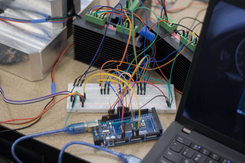 Astrobotics circuits An arduino circuit board connected to a breadboard with lots of wires connecting to other components, and a laptop on the right side of the image.