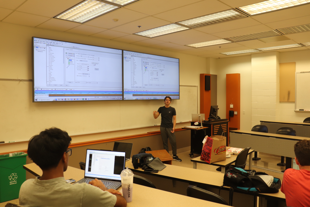 ASA presentation A student standing near a large screen addressing a small group of other students sitting at desks