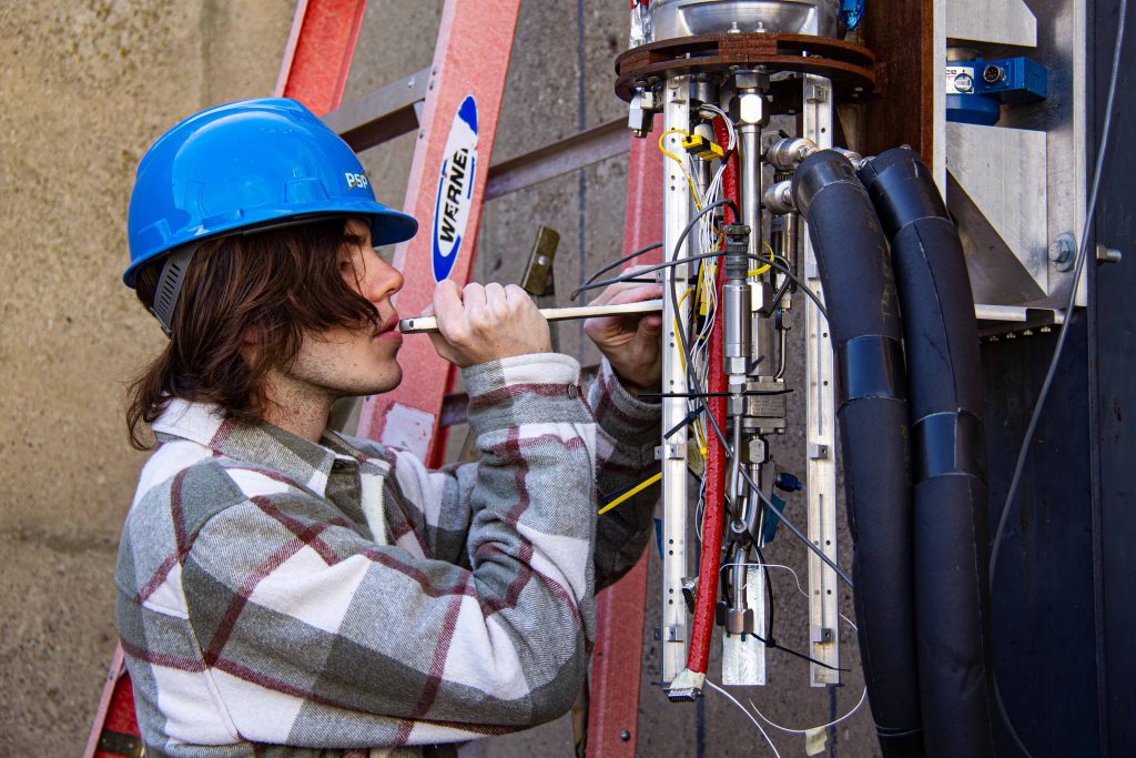 LQ wrench work A student wearing a blue hard hat holding a wrench working on the fluid systems of a liquid rocket