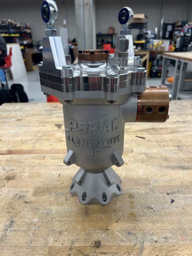 AC nozzle/chamber A large gray cylindrical part sits on a wooden workbench