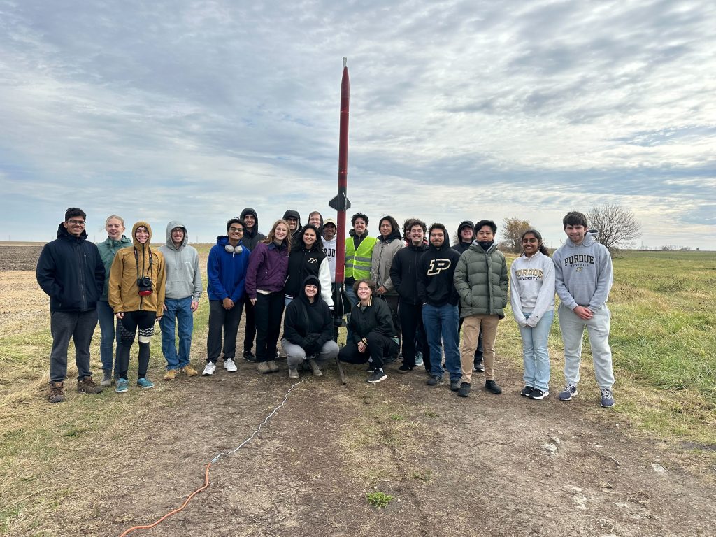 HA two stage team photo A group of students pose for a photo next to a red two stage rocket in a field