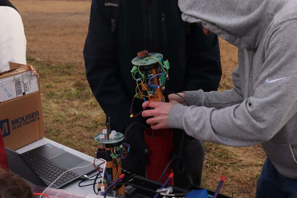 HA av bay launch photo Two students examine an avionics bay for a rocket at a table in a field