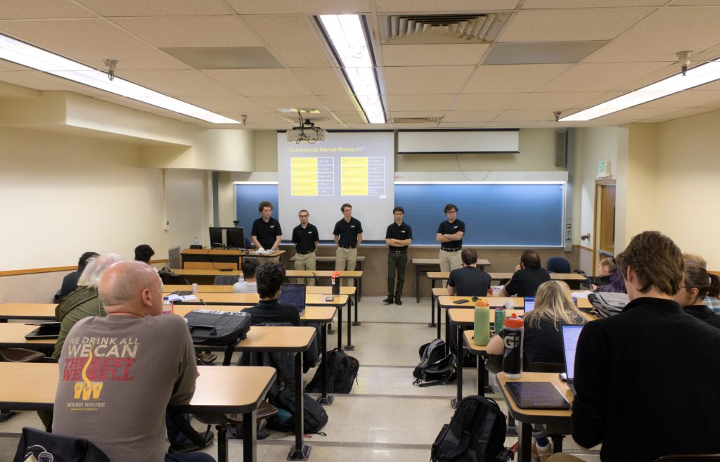 Sats presentation 2 Five students stand at the front of a classroom giving a presentation to a large group of observers